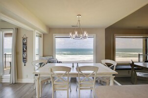 Un comedor con vista al océano, que cuenta con una mesa y sillas blancas, un candelabro y un ventanal grande.