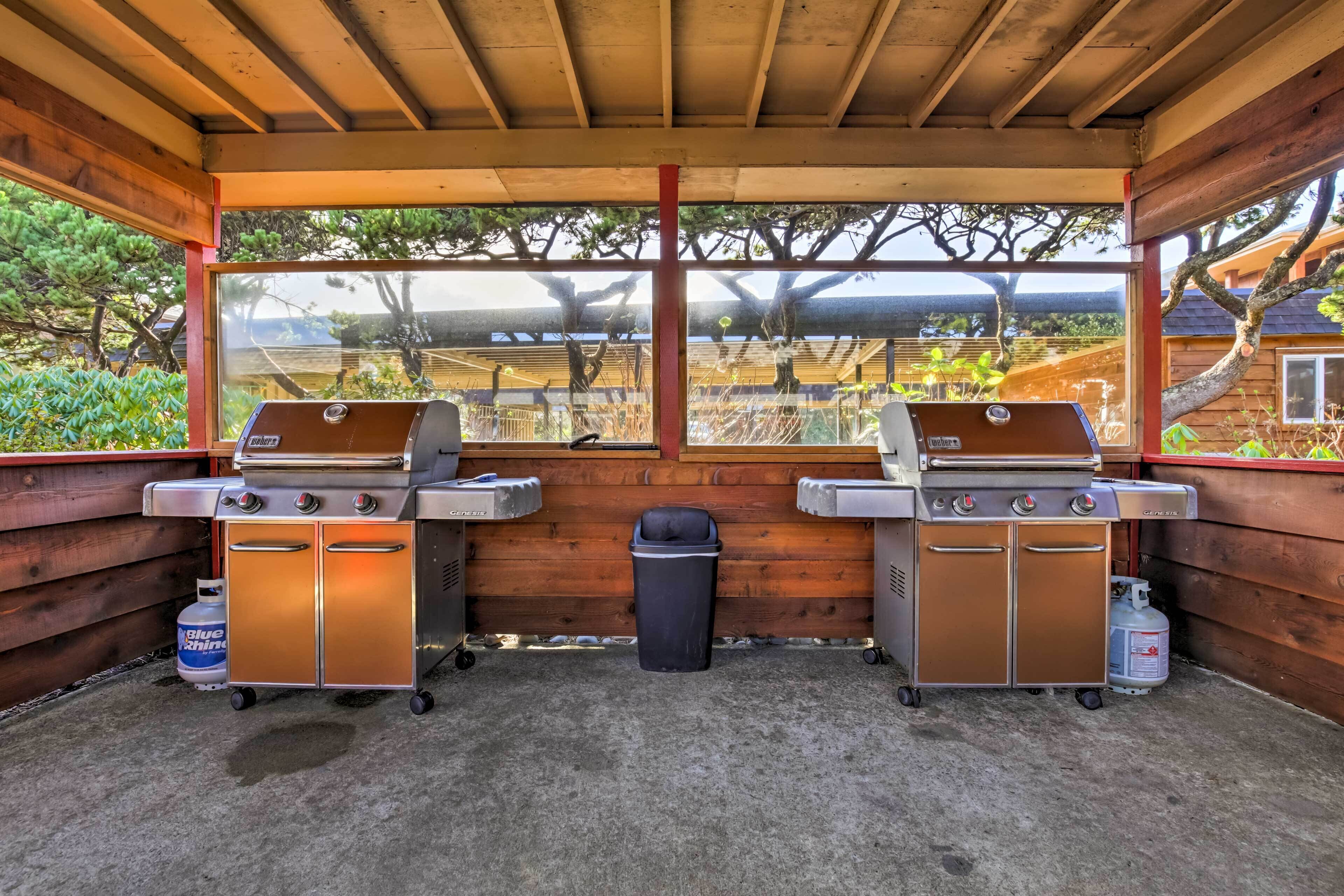 A covered outdoor area with two barbecue grills, a trash bin, and propane tanks.