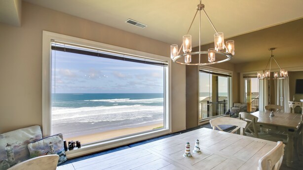 A dining area with a large window overlooking the beach, a chandelier, and a view of the ocean. - Oceanfront Oregon Retreat - Pool, Sauna & Patio! (Lincoln City)