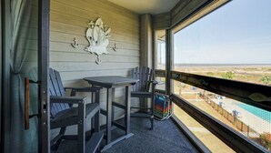 Ein Balkon mit Tisch und Stühlen, einem dekorativen Wandelement und Blick auf eine entfernte Landschaft.