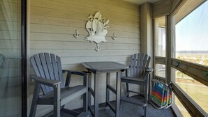 Ein Balkon mit zwei Adirondack-Stühlen, einem kleinen Tisch und einem dekorativen Wandgemälde mit einem Schiffsmotiv.