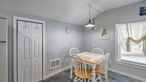 A dining area with a wooden table and white chairs, a clock on the wall, and a map. - Charming Studio < 10 Miles to Wells' Beaches! (Wells)