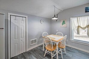 A dining area with a wooden table and white chairs, a clock on the wall, and a map. - Charming Studio < 10 Miles to Wells' Beaches! (Wells)