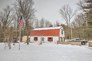 Une maison recouverte de neige, avec un toit rouge, une clôture en bois et un camionnette garée devant.