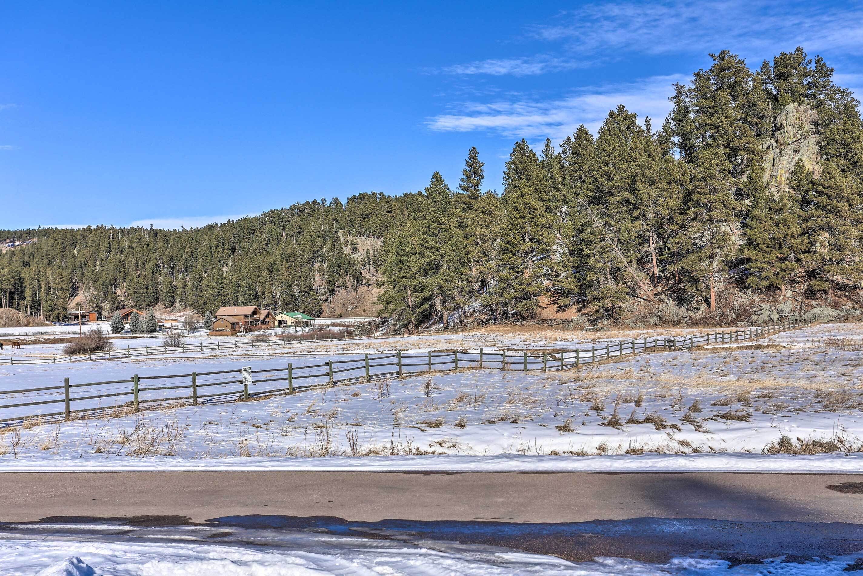 A snow-covered landscape with a wooden fence, a road, and a forest in the background.