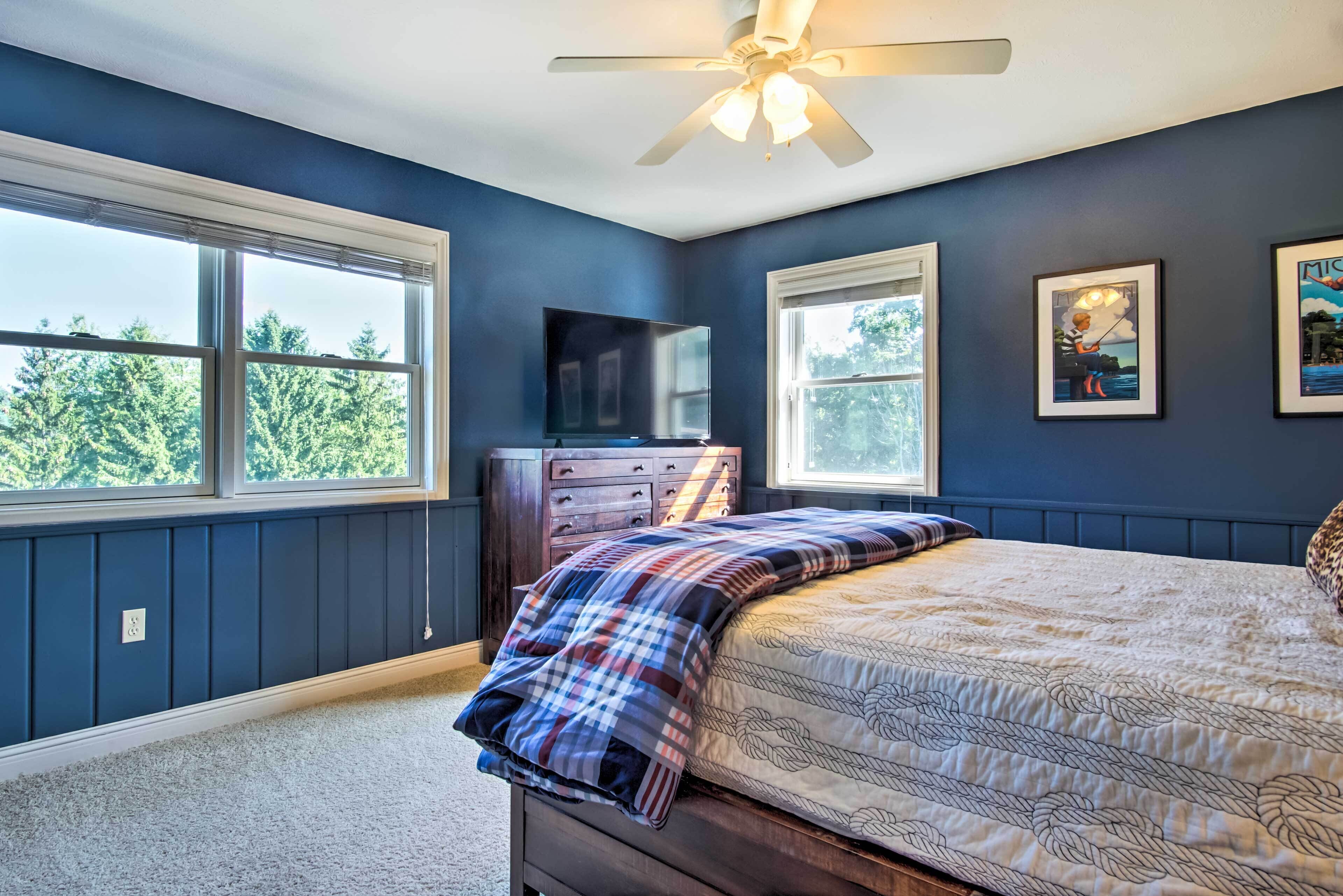 Une chambre à coucher avec un lit, une commode, un ventilateur de plafond et un téléviseur.