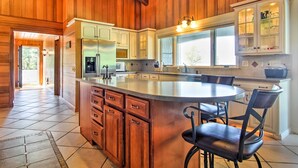 A spacious kitchen with wooden paneling, a large island with seating, and built-in cabinetry. - Hot Tub & Sauna! 7-acre Coastal Michigan Home (Ludington)