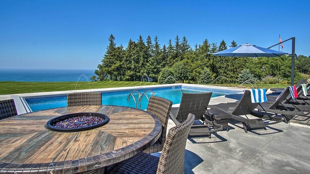 A poolside area with a view of the ocean, wicker furniture, and a flag. - Hot Tub & Sauna! 7-acre Coastal Michigan Home (Ludington)