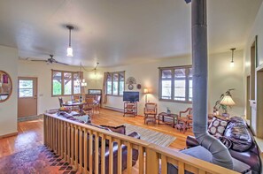 A spacious living room with a wooden floor, a large window, a fireplace, and a ceiling fan. - Bozeman Cottage w/ Mountain Views < 6 Mi to Dtwn! (Bozeman)