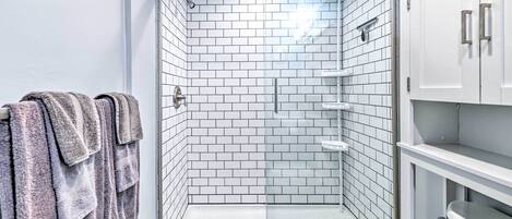 A modern bathroom with white tiled walls, a glass shower enclosure, and a white sink with a cabinet.