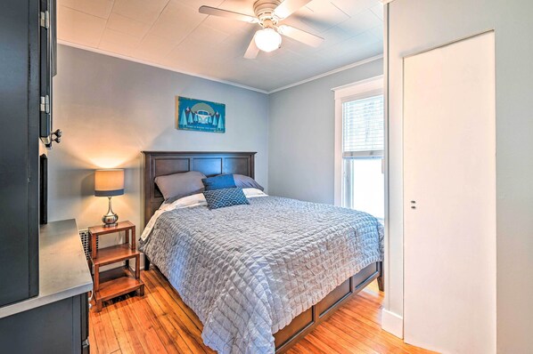 A bedroom with a bed, a nightstand, a ceiling fan, a window, and a door. - Cozy + Walkable Delmar Getaway w/ Fire Pit! (Delmar)
