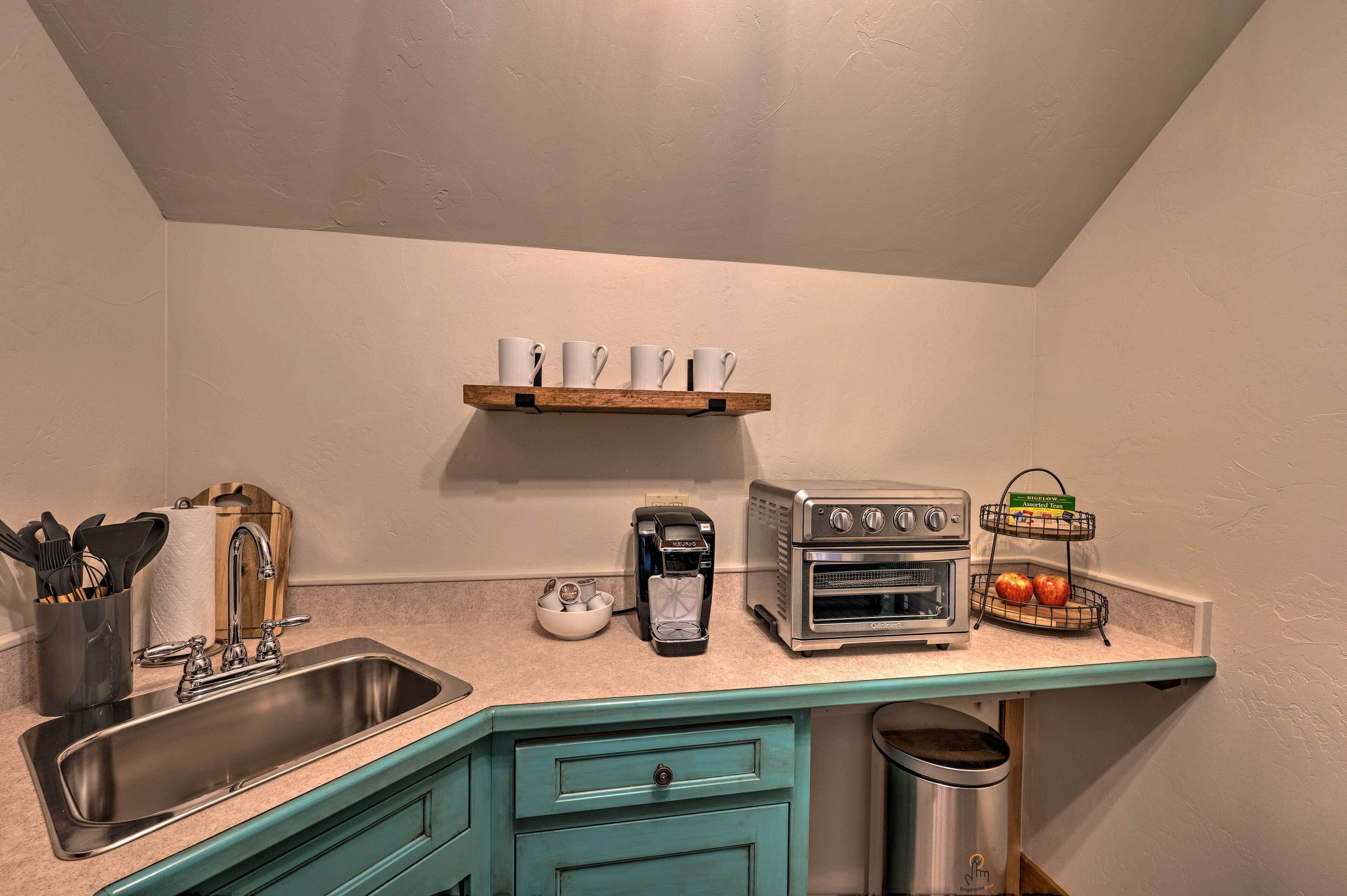 Cocina compacta con lavabo, cafetera, horno tostador y repisa con tazas.