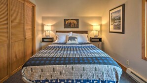A neatly made bed with a checkered bedspread, two bedside lamps, a wall-mounted picture, and a wooden wardrobe. - Private Mccall Apartment w/ Mountain View! (McCall)