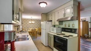 A compact kitchen with a sink, stove, microwave, and a dining area with chairs and a table. - Great Valley Home w/ On-site Pond, 7 Mi to Skiing! (Great Valley)