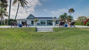 Ein modernes Haus mit Swimmingpool, umgeben von Palmen und einem gepflegten Rasen.