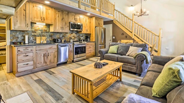 A spacious living area with a wooden coffee table, a sofa, and a staircase leading to an upper level. - Walk to Grand Lake: Riverfront Gem w/ Fireplace! (Grand Lake)
