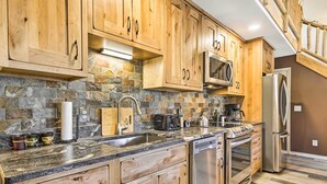 A kitchen with wooden cabinets, a stone backsplash, stainless steel appliances, and a granite countertop. - Walk to Grand Lake: Riverfront Gem w/ Fireplace! (Grand Lake)