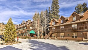 A snow-covered street with wooden buildings, including a lodge with a green awning and a staircase leading to the entrance. - Walk to Grand Lake: Riverfront Gem w/ Fireplace! (Grand Lake)