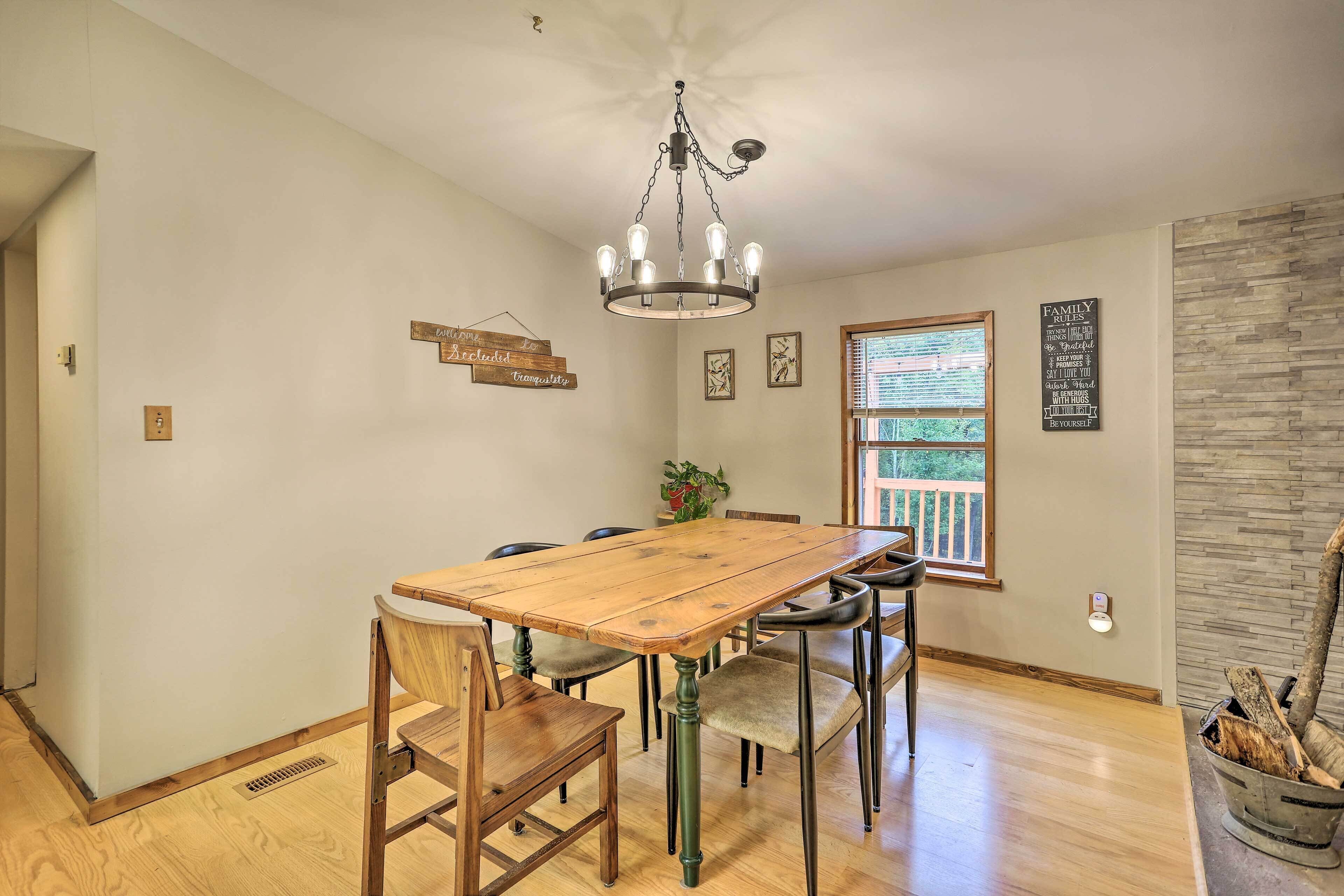A dining room with a wooden table and chairs, a chandelier, a window with blinds, and a stone accent wall.