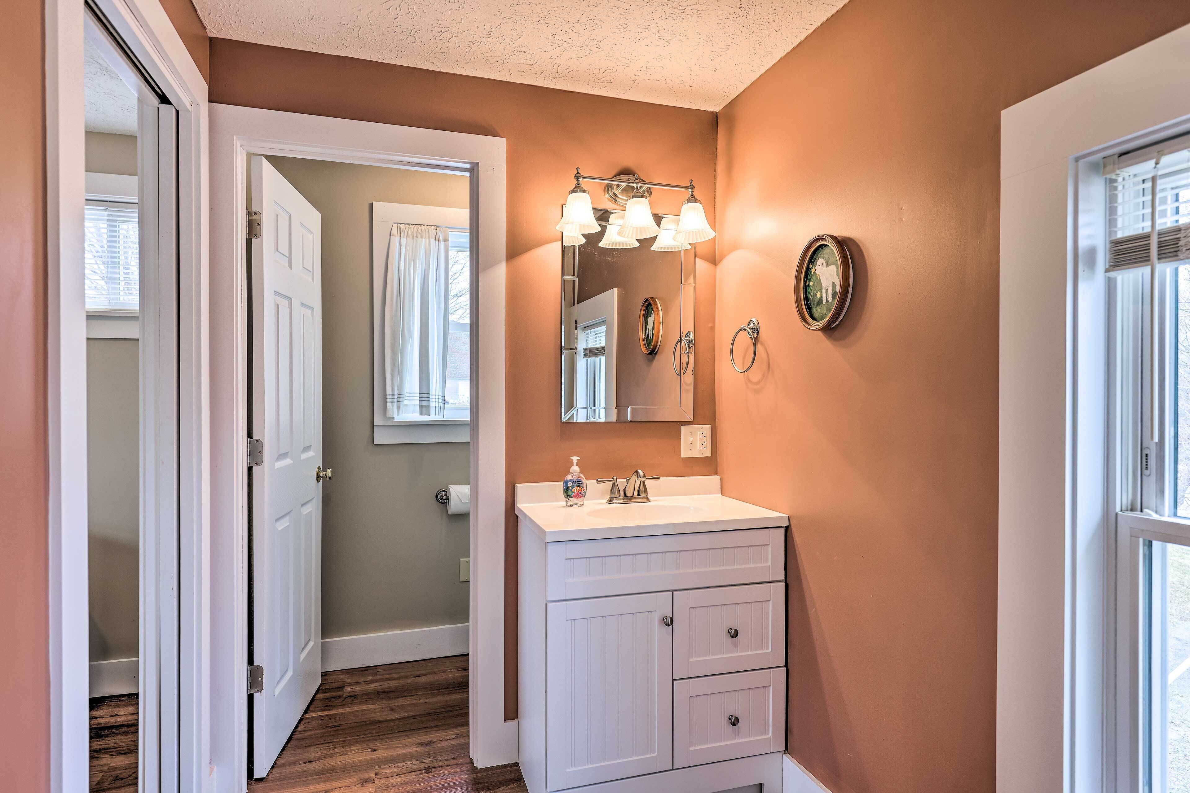 Une salle de bain avec un meuble-lavabo blanc, un miroir avec éclairage intégré et un porte-serviettes.