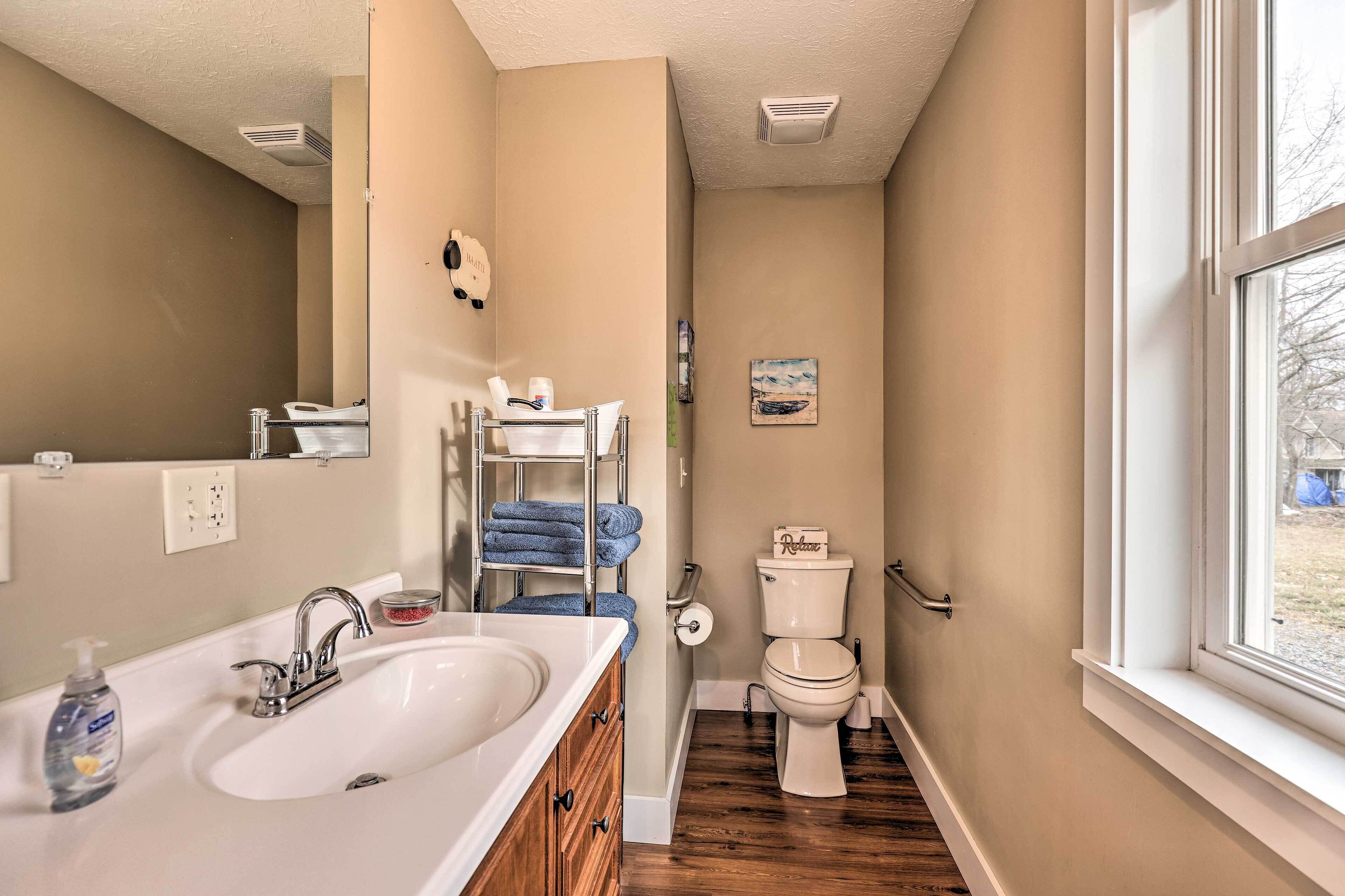 A bathroom with a white sink, a mirror, a towel rack with blue towels, a toilet, and a window.