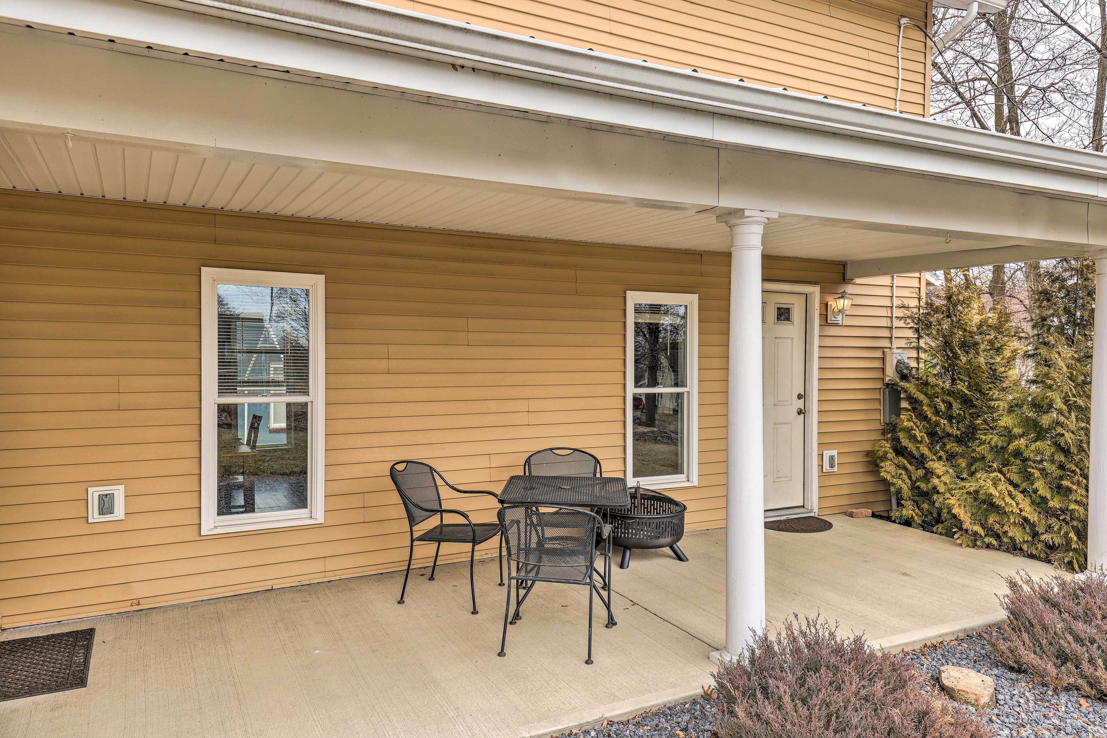 A covered porch with a table and chairs, a door, and a small garden area with rocks and plants.