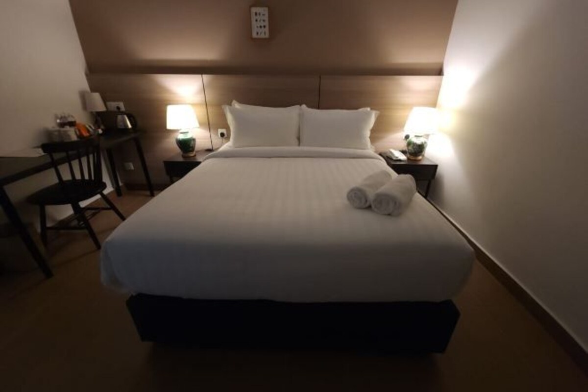 Una habitación de hotel con una cama grande, dos mesitas de noche, una silla y dos lámparas.