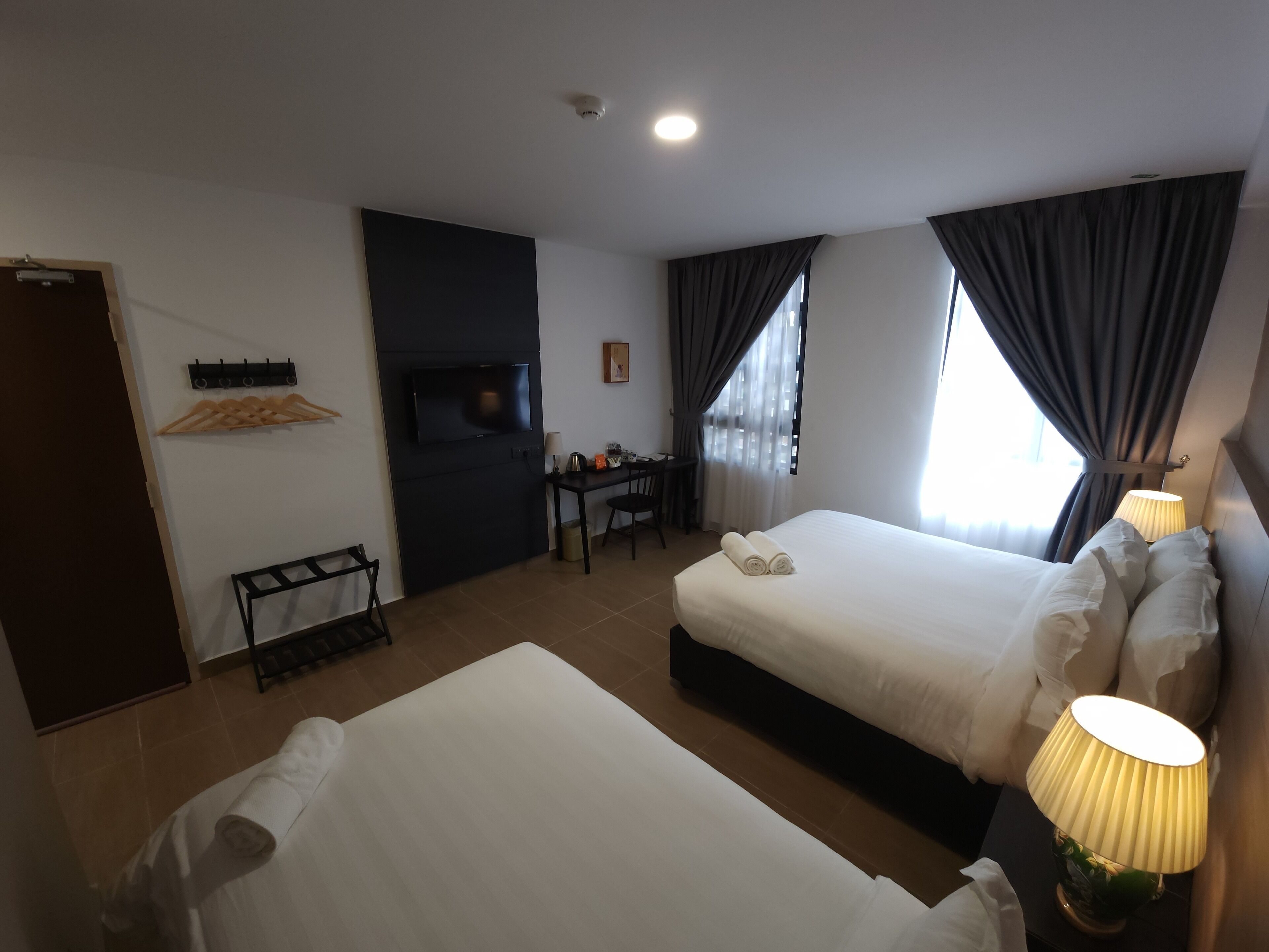 A hotel room with two beds, a desk, a TV, and a window with curtains.