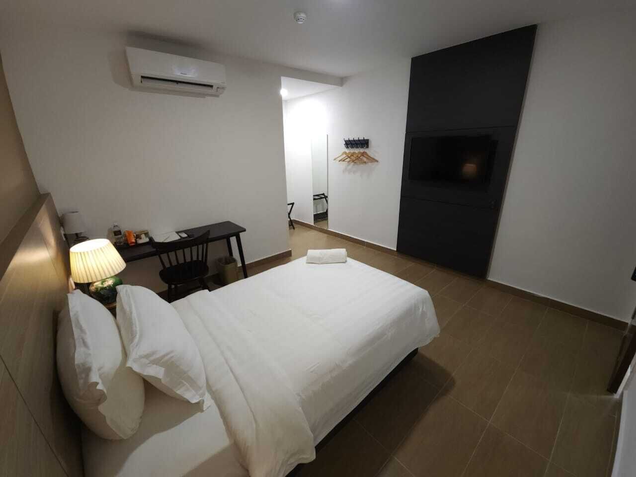Quarto de hotel com cama, escrivaninha, cadeira, luminária, ar condicionado e televisão.