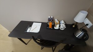 A small table with a remote control, a notebook, a pen, two bottles, a tissue box, a teapot, a lamp, and a power outlet. - Yu Hotel Chinatown (Kuala Lumpur)