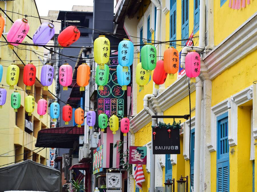 Una calle con faroles y letreros coloridos, que muestra un barrio lleno de vida.