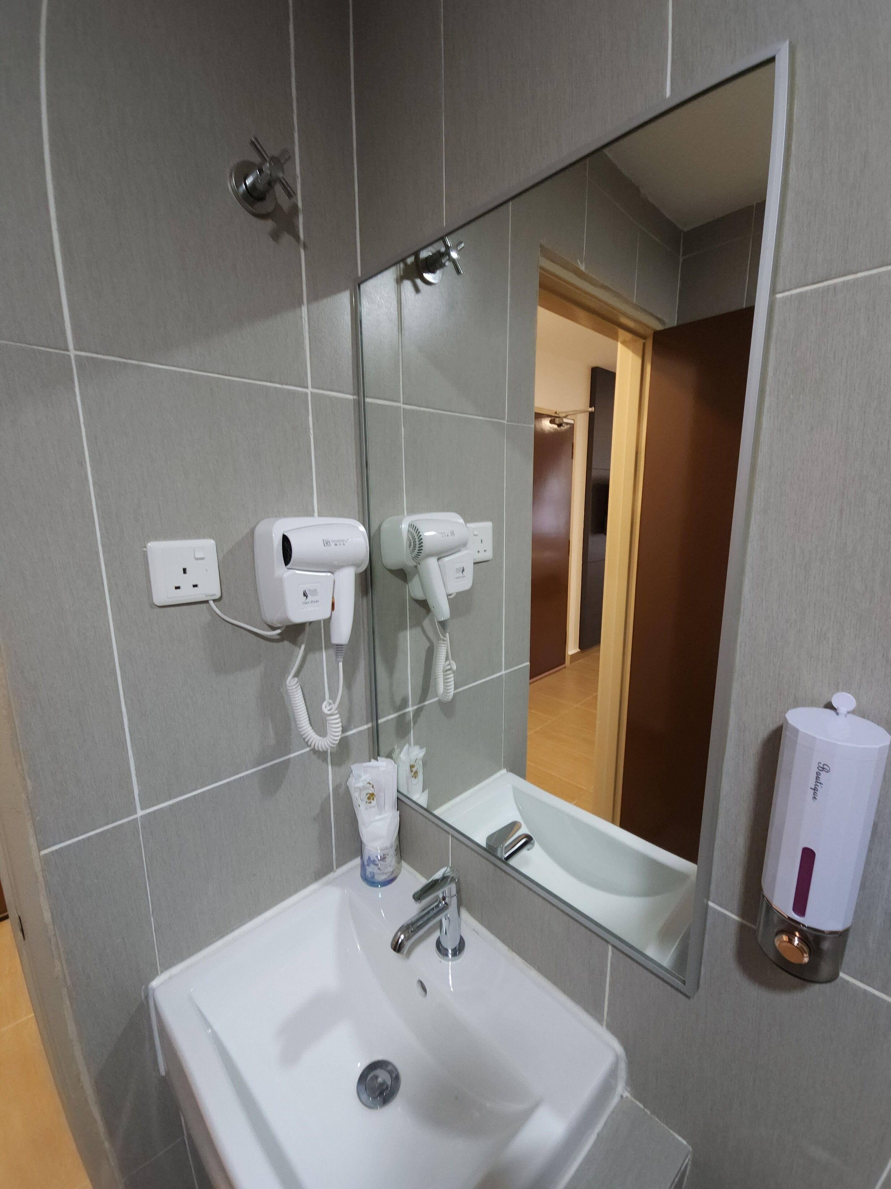 A bathroom with a white sink, a mirror, and two hair dryers mounted on the wall.