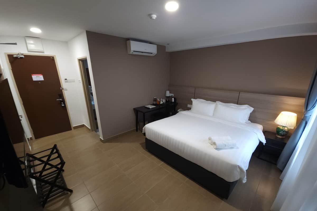A hotel room with a large bed, a desk, a chair, an air conditioning unit, and a door.