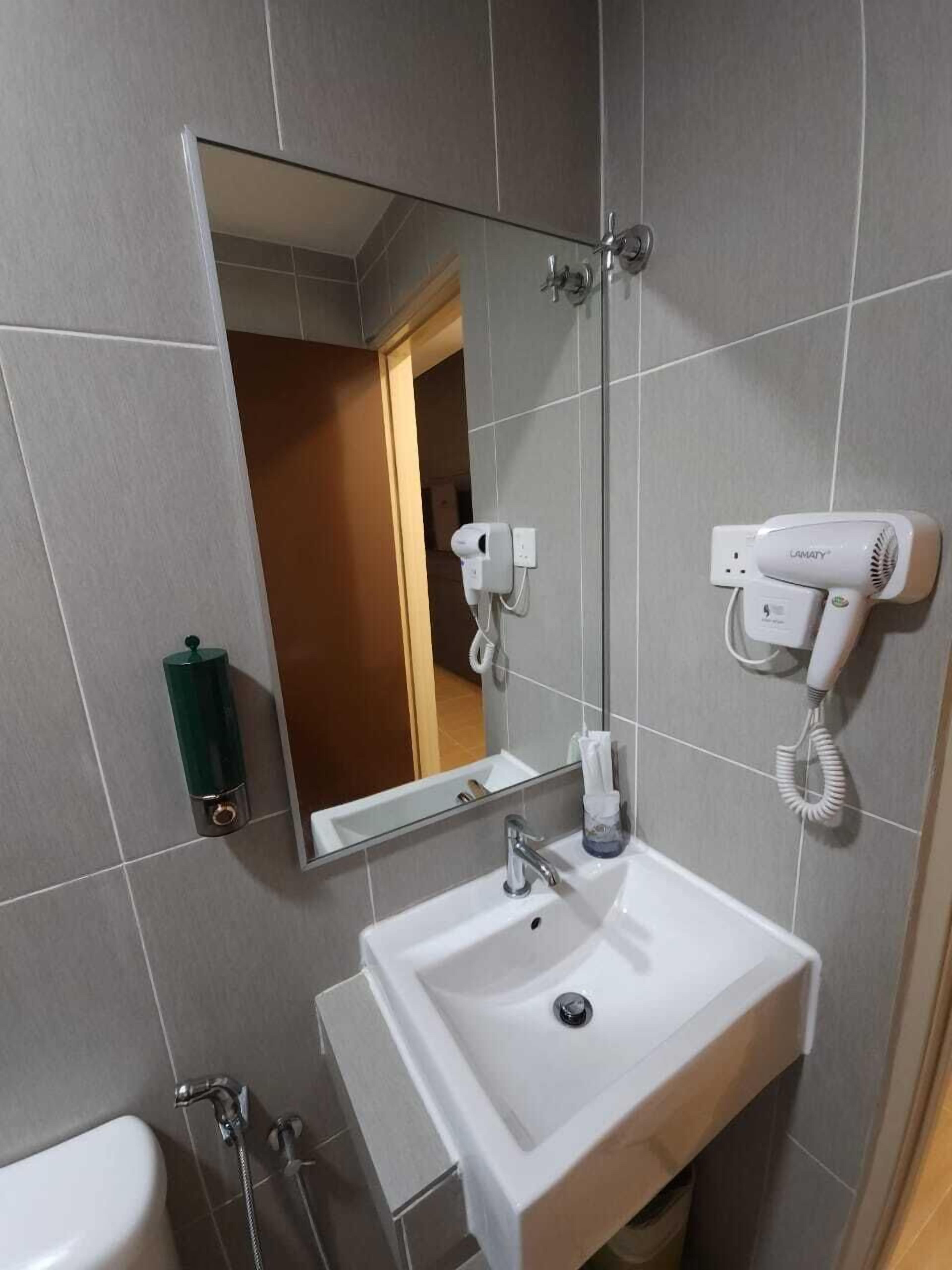 A bathroom with a white sink, a mirror, a handheld hair dryer, and a towel dispenser.