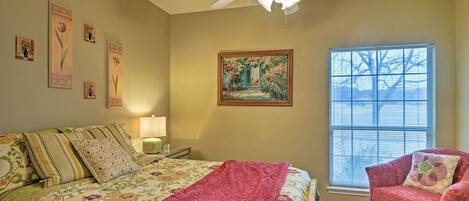 A bedroom with a bed, a chair, a window with blinds, a ceiling fan, and wall art.