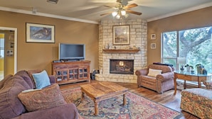 A living room with a stone fireplace, a ceiling fan, and a large window. - Round Rock Lakefront Home w/ Water Toys & Fire Pit (Round Rock)