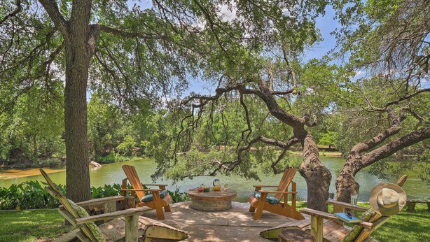 A wooden deck with Adirondack chairs, a fire pit, and a view of a pond surrounded by trees. - Round Rock Lakefront Home w/ Water Toys & Fire Pit (Round Rock)