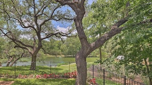 A park with mature trees, a fenced area, and a body of water in the background. - Round Rock Lakefront Home w/ Water Toys & Fire Pit (Round Rock)