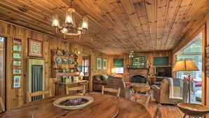 Ein gemütliches Holzhaus-Interieur mit Esstisch, Stühlen, Kamin und verschiedenen gerahmten Bildern und Dekorationen.