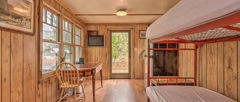 A wooden cabin with a bunk bed, a desk with a chair, and a television.