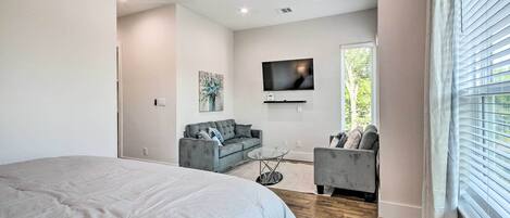 A modern bedroom with a large bed, a grey sofa, a small coffee table, and a TV mounted on the wall.