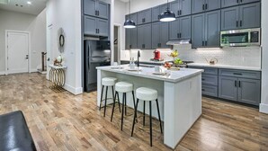 A modern kitchen with grey cabinets, a central island with stools, a microwave, and a refrigerator. - Game Day Ready Home: 2 Mi to Dtwn Houston (Houston)