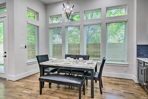 A dining area with a table set for four, large windows with blinds, and a chandelier. - Modern Home w/ Yard: 2 Mi to Downtown Houston! (Houston)