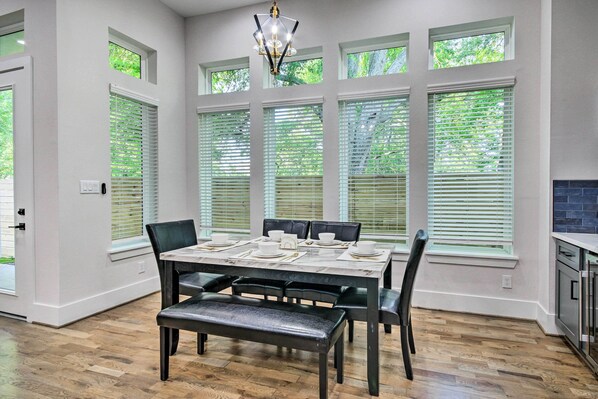 A dining area with a table set for four, large windows with blinds, and a chandelier.