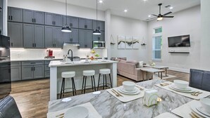 A modern kitchen with grey cabinets, a central island with stools, and a dining area set for six with white plates and gold cutlery. - Game Day Ready Home: 2 Mi to Dtwn Houston (Houston)