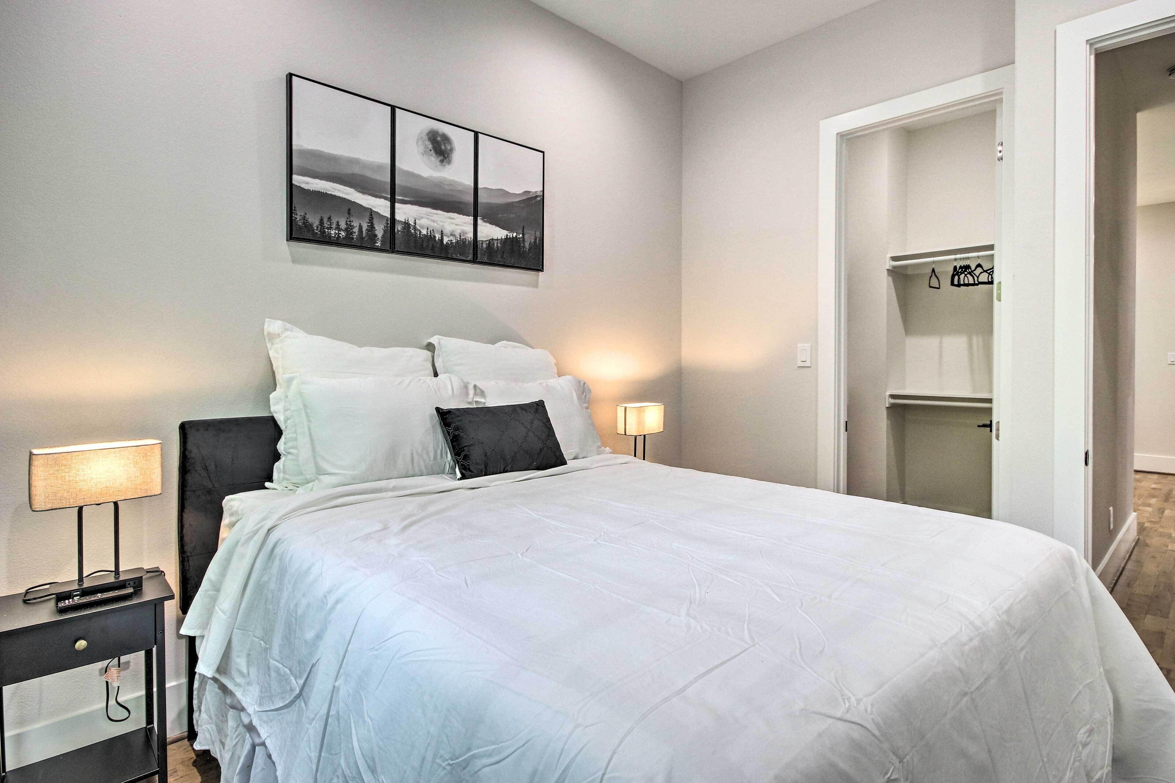 A neatly made bed with white bedding, a black headboard, and a wall-mounted picture of a landscape.