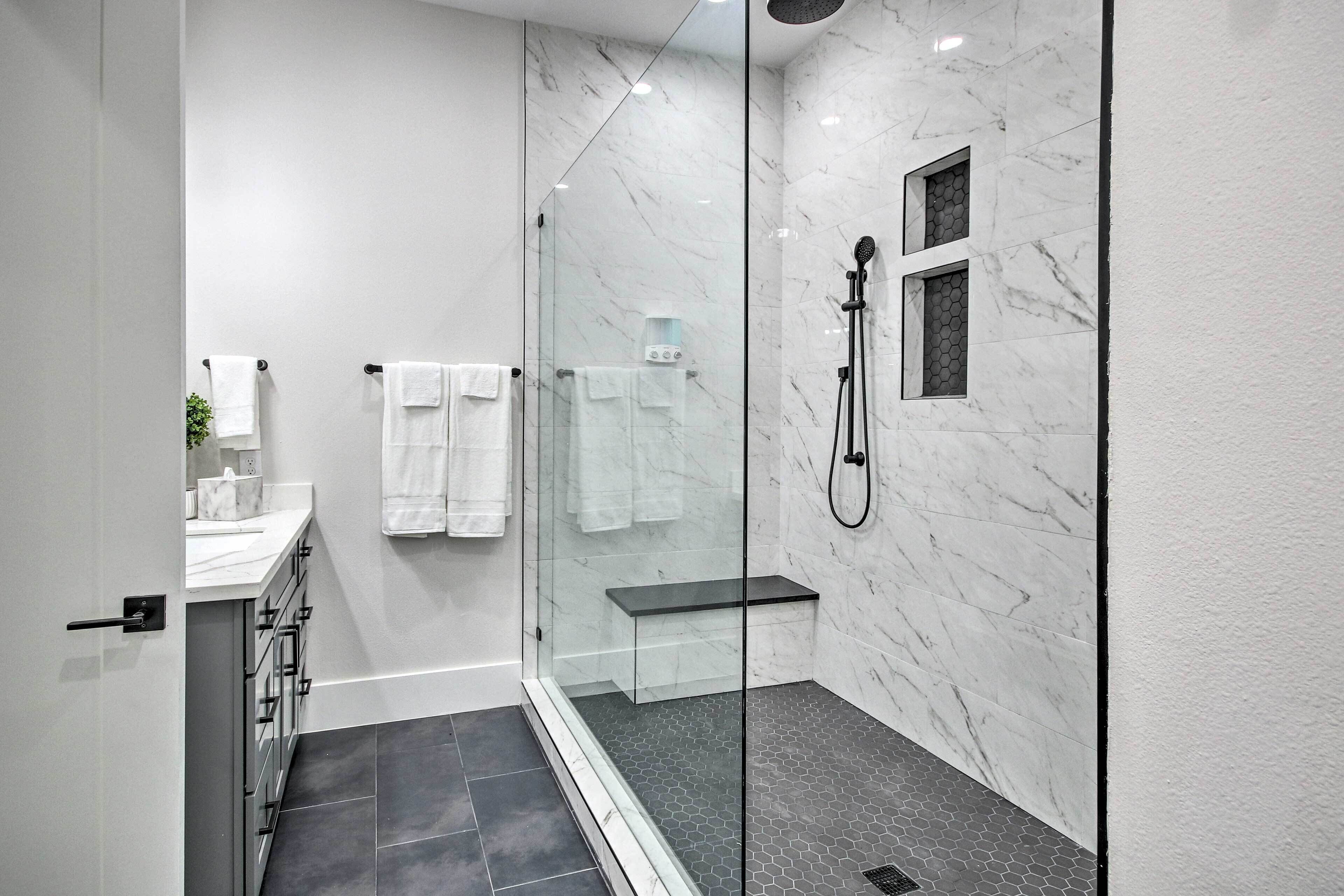 A modern bathroom with a glass-enclosed shower, marble walls, and a black tiled floor.