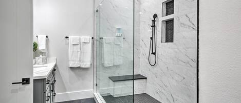 A modern bathroom with a glass-enclosed shower, marble walls, and a black tiled floor.