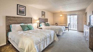 A hotel room with two beds, a wooden headboard, a desk with a chair, a television, and a door leading to a balcony.