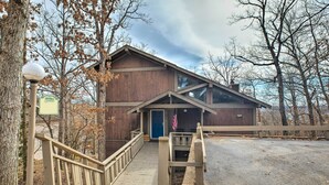 A wooden lodge with a wooden staircase leading to a blue door, an American flag, and a signboard.